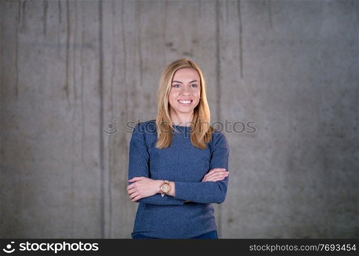 portrait of young successful smiling casual businesswoman standing in front of a concrete wall at new startup office