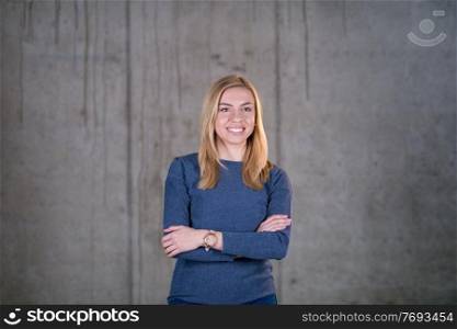 portrait of young successful smiling casual businesswoman standing in front of a concrete wall at new startup office