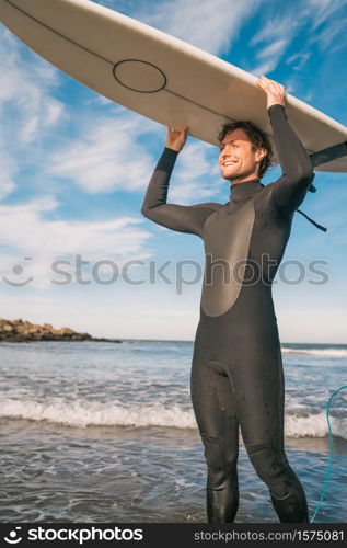 Portrait of young surfer at the beach holding up his surfboard and wearing a black surfing suit. Sport and water sport concept.