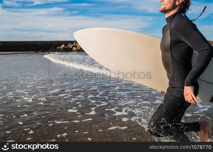 Portrait of young surfer leaving the water with surfboard under his arm. Sport and water sport concept.