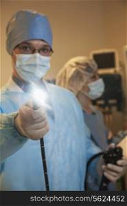 Portrait of young surgeon holding a medical instrument towards the camera, light shining
