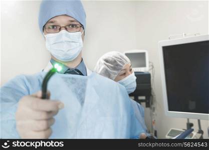Portrait of young surgeon holding a medical instrument towards the camera, light shining