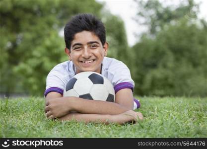 Portrait of young teenage boy with soccer ball lying on grass
