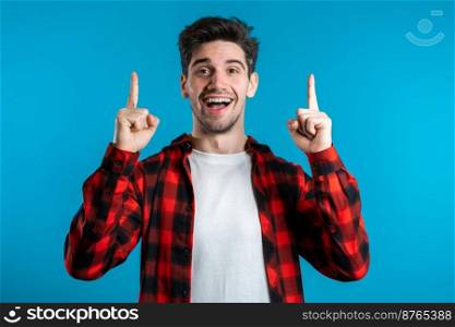Portrait of young thinking pondering man in red having idea moment pointing finger up on blue studio background. Smiling happy student guy showing eureka gesture. Portrait of young thinking pondering man in red having idea moment pointing finger up on blue studio background. Smiling happy student guy showing eureka gesture.