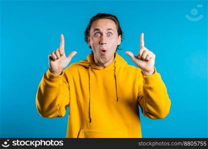 Portrait of young thinking pondering man in yellow having idea moment pointing finger up on blue studio background. Smiling happy student guy showing eureka gesture. High quality photo. Portrait of young thinking pondering man in yellow having idea moment pointing finger up on blue studio background. Smiling happy student guy showing eureka gesture.