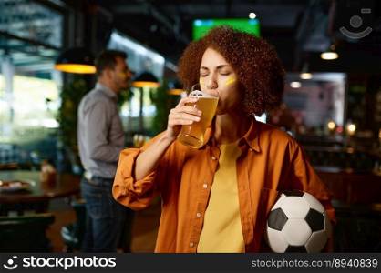 Portrait of young thirsty girl football fan drinking beer while rest and spend time with friends in sports bar. Young girl football fan drinking beer while rest in sports bar with friends