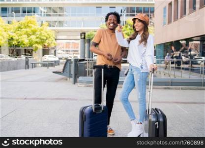 Portrait of young tourist couple carrying suitcase while standing outside airport or train station. Tourism concept.