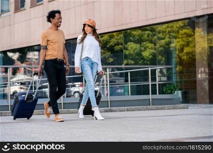 Portrait of young tourist couple carrying suitcase while walking outdoors on the street. Tourism concept.