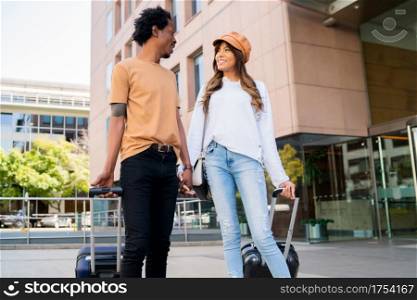 Portrait of young tourist couple carrying suitcase while walking outdoors on the street. Tourism concept.