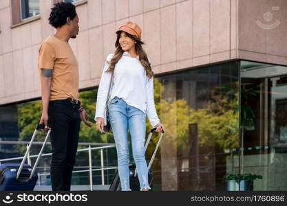 Portrait of young tourist couple carrying suitcase while walking outdoors on the street. Tourism concept.