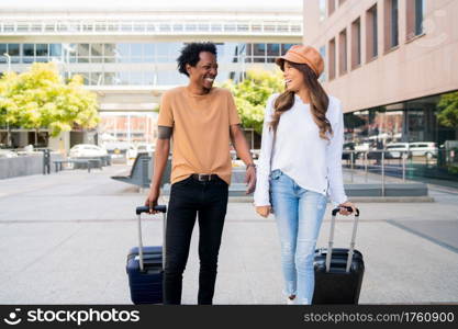 Portrait of young tourist couple carrying suitcase while walking outdoors on the street. Tourism concept.