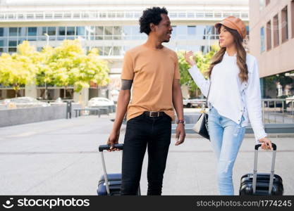 Portrait of young tourist couple carrying suitcase while walking outdoors on the street. Tourism concept.. Tourist couple carrying suitcase while walking outdoors.