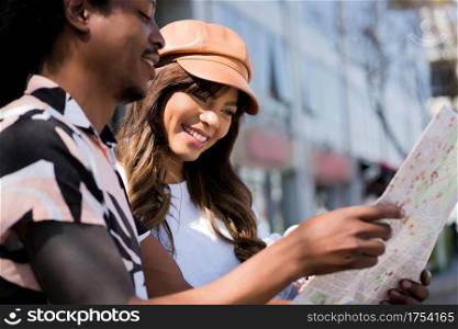 Portrait of young tourist couple using map and looking for directions while walking outdoors. Tourism concept.