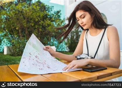 Portrait of young tourist woman with a map and looking for directions while sitting at coffee shop. Travel concept.