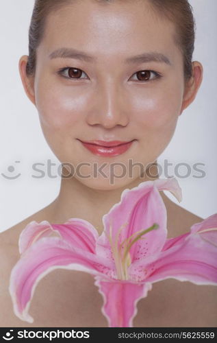 Portrait of young tranquil woman looking at camera with a large pink flower, studio shot