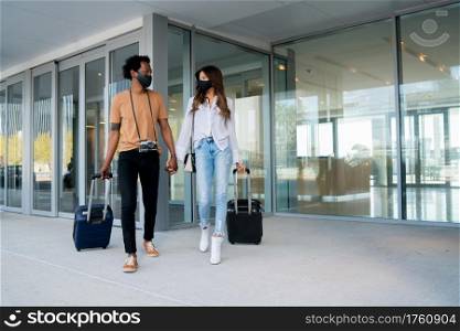 Portrait of young traveler couple wearing protective mask and carrying suitcase while walking outdoors on the street. Tourism concept. New normal lifestyle concept.