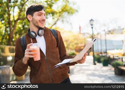 Portrait of young traveler man holding a map and looking for directions while drinking fresh fruit juice. Travel and holiday concept.