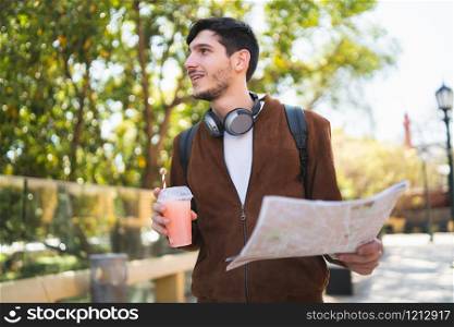 Portrait of young traveler man holding a map and looking for directions while drinking fresh fruit juice. Travel and holiday concept.
