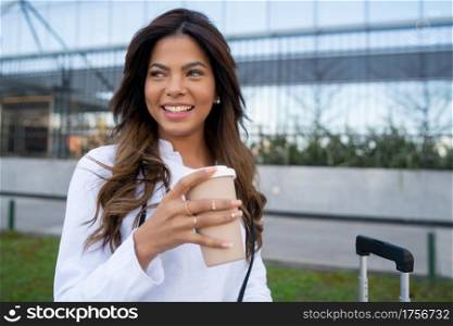 Portrait of young traveler woman holding a cup of coffee while sitting outdoors on the street. Urban concept. Tourism concept.
