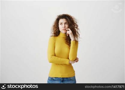 Portrait of young tricky woman touching lock of hair meaning she has something in mind with facial expressions, over gray background. Portrait of young tricky woman touching lock of hair meaning she has something in mind with facial expressions, over gray background.