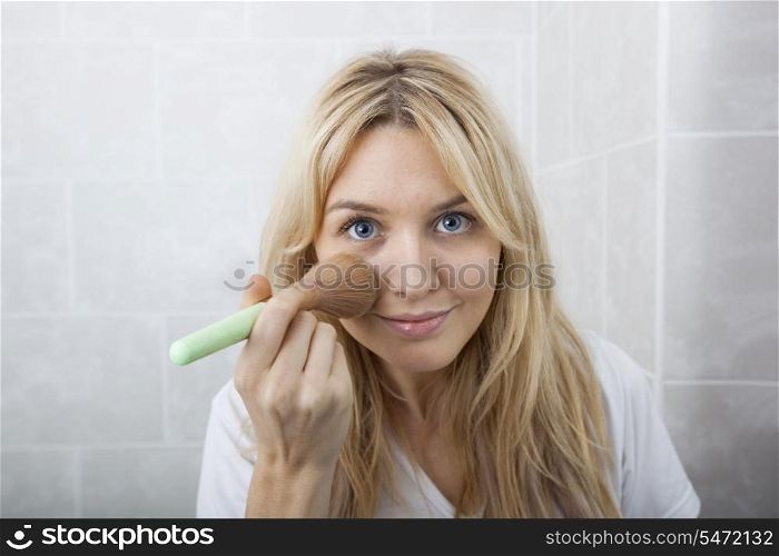 Portrait of young woman applying blush in bathroom