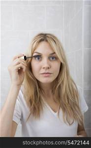 Portrait of young woman applying mascara in bathroom