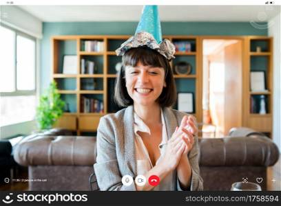 Portrait of young woman celebrating birthday on a video call from home. Woman celebrating birthday online in quarantine time. New normal lifestyle concept.