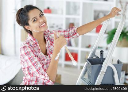 portrait of young woman climbing step ladder to paint wall