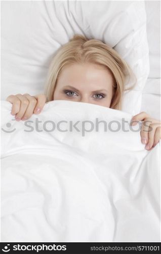 Portrait of young woman covering face with bed sheet
