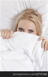 Portrait of young woman covering face with bed sheet