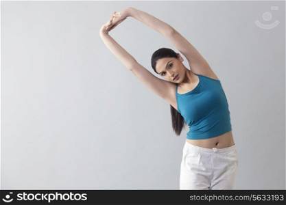 Portrait of young woman doing stretching exercise isolated over gray background