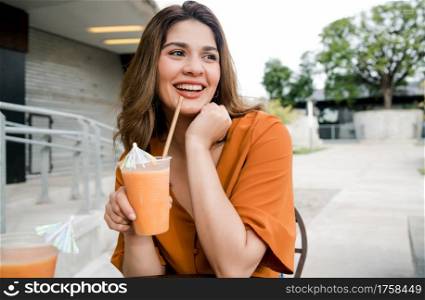 Portrait of young woman drinking a fresh juice fruit at a coffee shop outdoors. Urban concept.