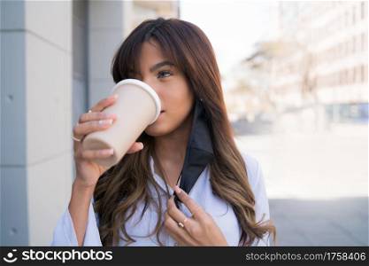 Portrait of young woman drinking coffee while standing outdoors on the street. Urban concept.