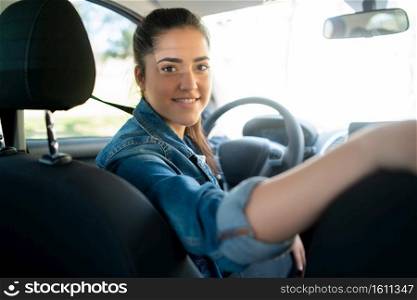 Portrait of young woman driving her car and looking at back seat to camera. Transport concept.. Woman driving her car and looking at back seat