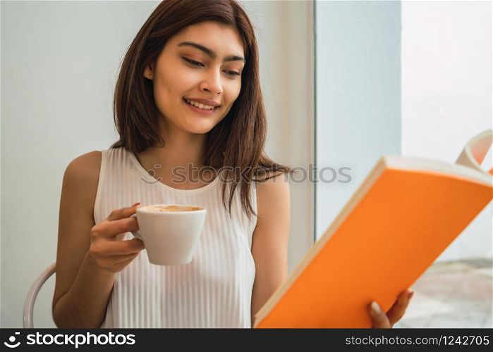 Portrait of young woman enjoying free time and reading a book while sitting outdoors at coffee shop.