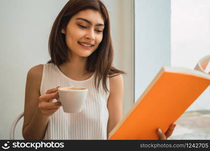Portrait of young woman enjoying free time and reading a book while sitting outdoors at coffee shop.