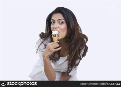 Portrait of young woman enjoying ice-cream cone over white background