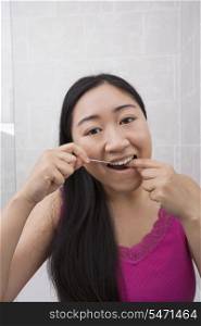 Portrait of young woman flossing her teeth in bathroom