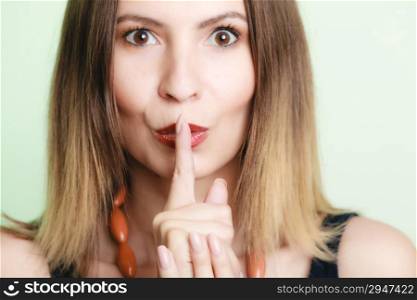 Portrait of young woman. Girl asking for silence or secrecy with finger on lips hush hand gesture on green