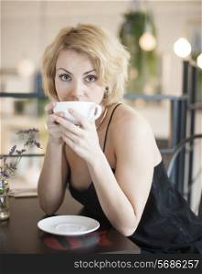 Portrait of young woman having coffee at restaurant table