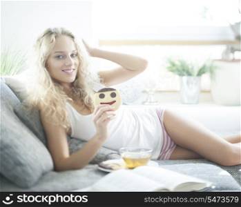 Portrait of young woman having cookie while relaxing on sofa