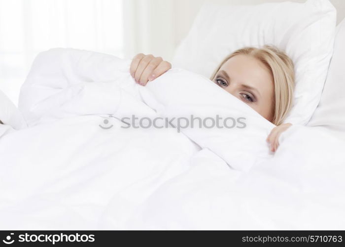 Portrait of young woman hiding under bedsheet