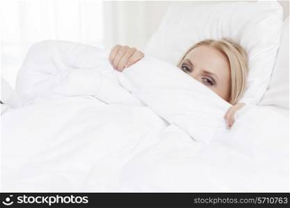 Portrait of young woman hiding under bedsheet