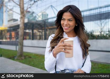 Portrait of young woman holding a cup of coffee while sitting outdoors on the street. Urban concept.