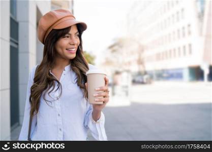 Portrait of young woman holding a cup of coffee while walking outdoors on the street. Urban concept.