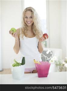 Portrait of young woman holding apples at kitchen counter
