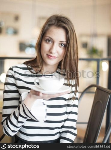 Portrait of young woman holding coffee cup and saucer at cafe