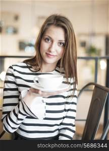Portrait of young woman holding coffee cup and saucer at cafe