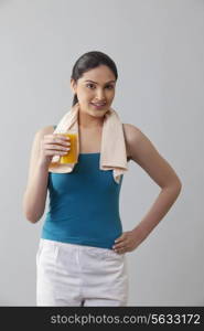 Portrait of young woman holding glass of orange juice against gray background