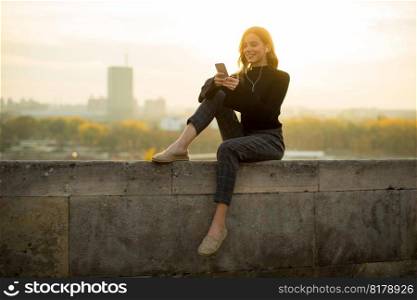 Portrait of young woman holding mobile phone while sitting on the wall